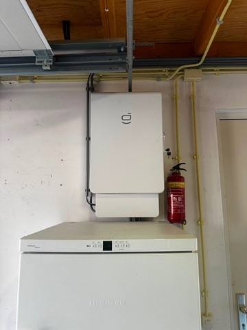 Sigenergy omvormer met Sigen Gateway aan de wand in een garage, naast een brandblusser