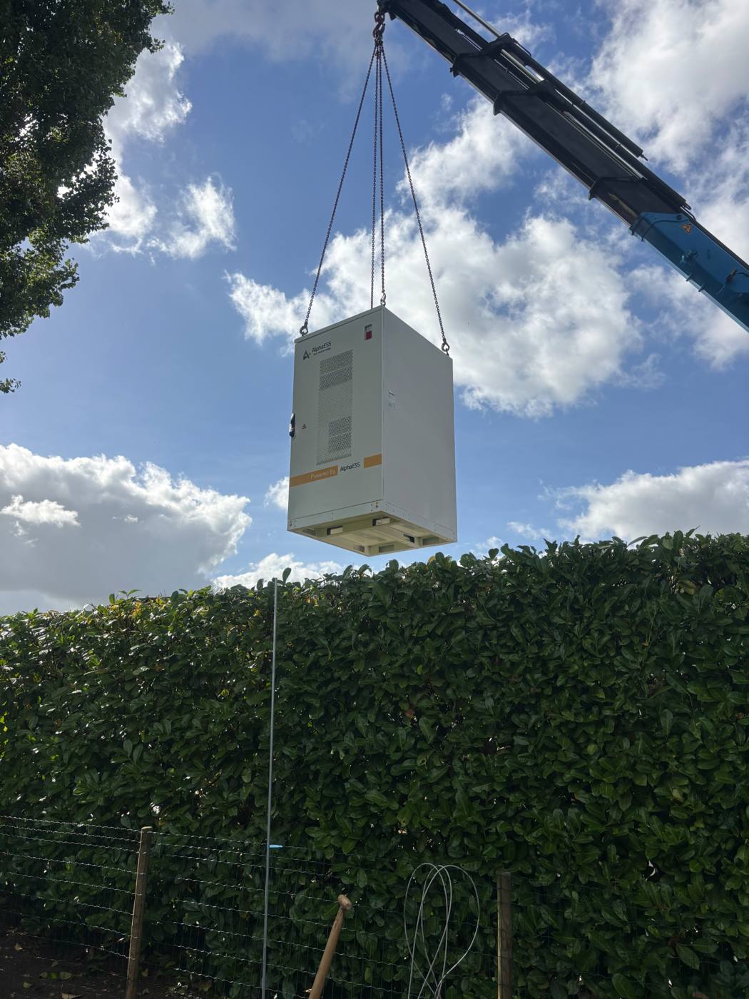 AlphaESS STORION H50 bedrijfsbatterij wordt met een kraan over een haag gehesen