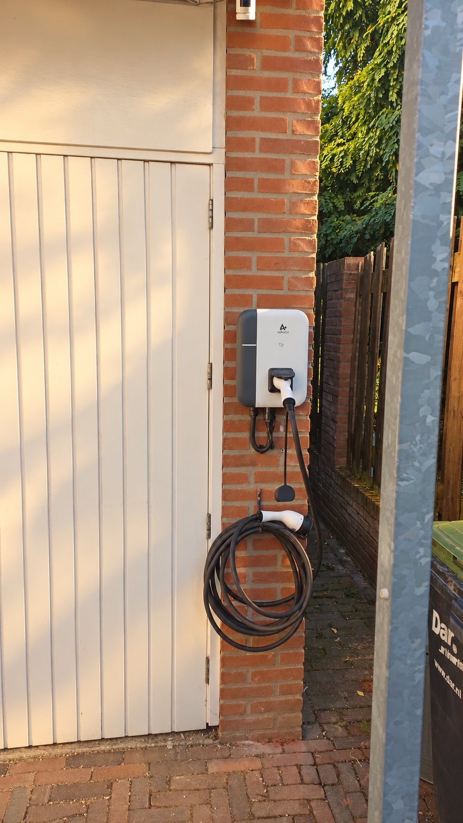 AlphaESS laadpaal met vaste kabel aan een bakstenen garage in de avondzon