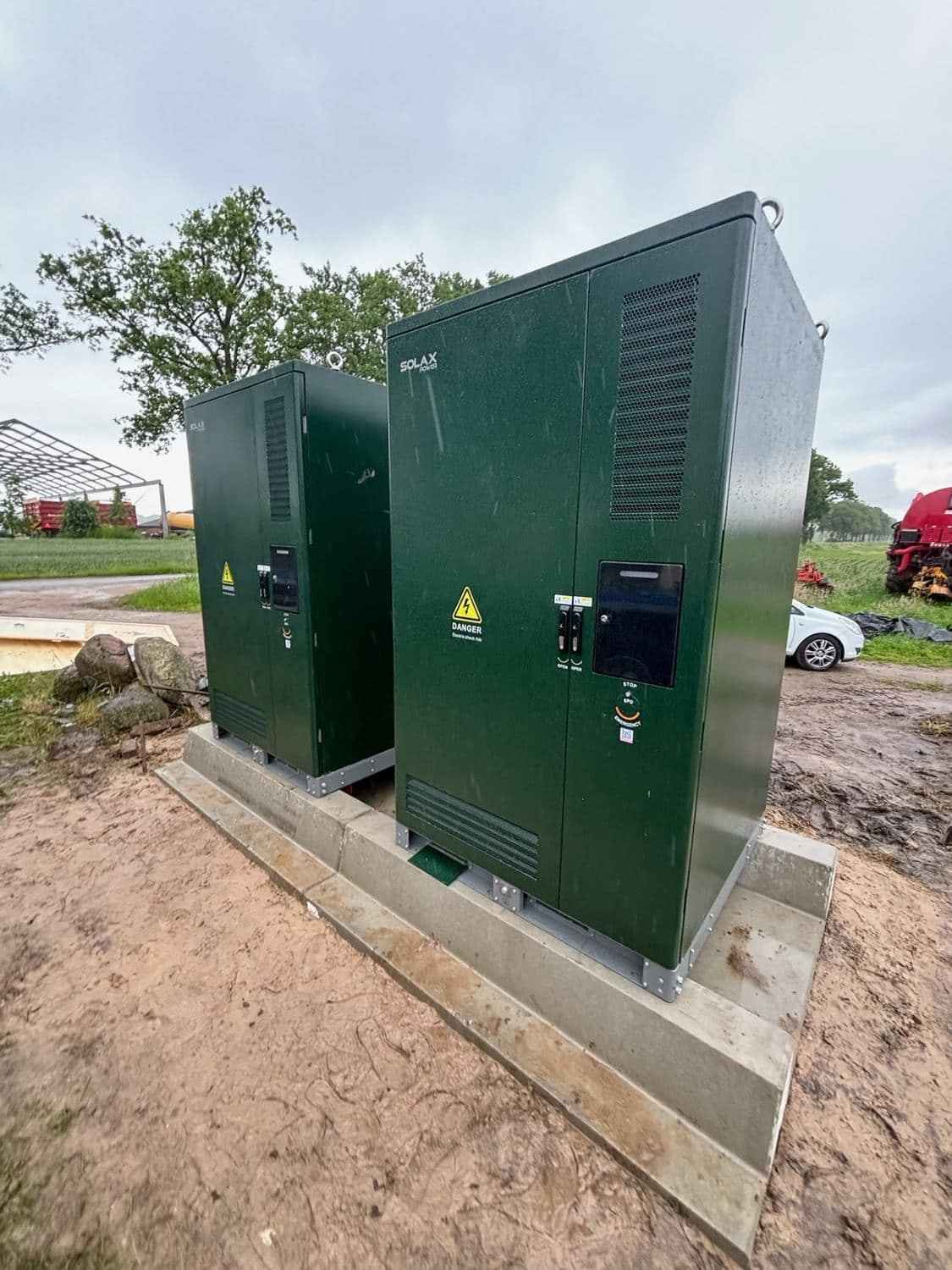 Twee groene SolaX batterijkasten op een betonnen fundering bij een agrarisch bedrijf